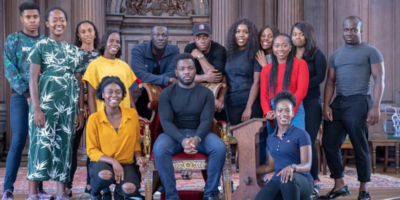 Stormzy seated and surrounded by students from the University of Cambridge Afro-Caribbean Society